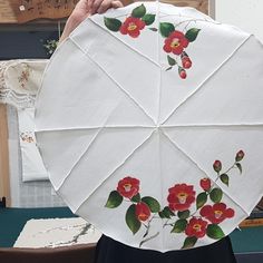 a woman holding up a white umbrella with red flowers on the outside and green leaves on the inside