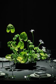 the table is set with plates, silverware and green plants