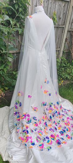 a white wedding dress with colorful butterflies on it and a veil draped over the back