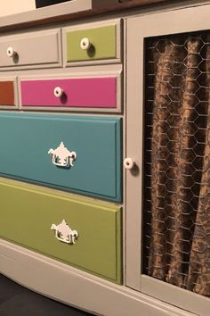 the drawers are painted different colors and have decorative knobs on each drawer, along with a chicken wire curtain