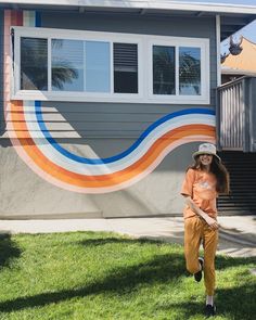 a woman standing in front of a house with a mural on the side of it