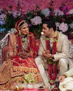 a man and woman sitting next to each other on a couch in front of flowers