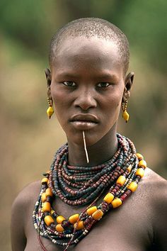 an african woman with necklaces on her neck and nose ring, looking at the camera