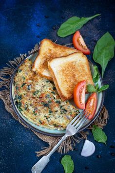 two pieces of toast on a plate with tomatoes and spinach leaves next to it