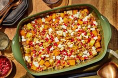 a green casserole dish filled with food on top of a wooden table next to other dishes