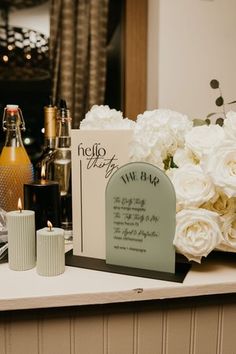 a table topped with flowers and candles next to a bottle of wine on top of a counter