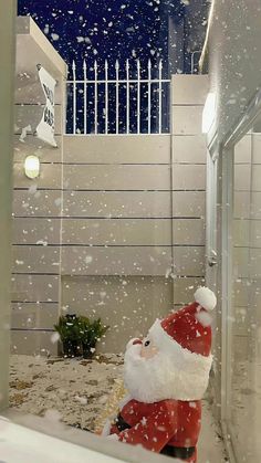 a santa clause statue in front of a window with snow falling on it and a white picket fence