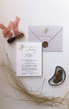 the wedding stationery is laid out on top of some dried grass and pink ribbon