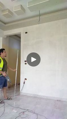 a man in a yellow vest is painting a room with white walls and electrical wires