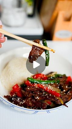 someone holding chopsticks above a bowl of food with meat and vegetables on it