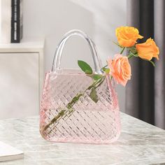 a pink handbag sitting on top of a table next to orange flowers and a laptop