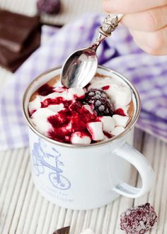 a person spooning some ice cream into a cup filled with raspberries and marshmallows