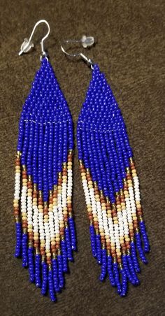 Bohemian hand beaded tassel earrings in royal blue , gold,  brown,  tan and white.  A large royal blue diamond is set off with strands of gold,  brown,  tan and white in these 4 inch long and 1 inch wide earrings. Blue Beaded Fringe Tassel Earrings For Festivals, Blue Fringed Beaded Earrings For Festival, Elegant Blue Tassel Earrings For Festival, Bohemian Blue Earrings With Beaded Fringe, Bohemian Blue Earrings With Fringe, Blue Bohemian Earrings With Fringe, Adjustable Blue Tassel Earrings With Colorful Beads, Traditional Blue Beaded Fringe Earrings, Blue Tassel Earrings For Festivals