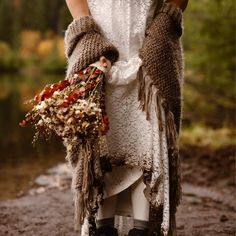 a woman in a white dress holding a bouquet of flowers and wearing gloves with her arms wrapped around her body