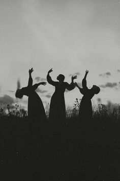 three people standing on top of a grass covered field with their arms in the air