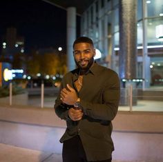 a man standing in front of a building at night with his hands clasped to his chest