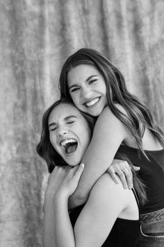 two young women hugging each other in front of a curtain