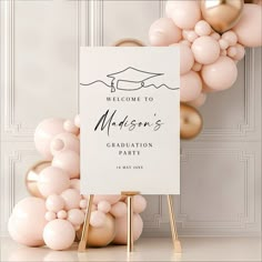 a welcome sign surrounded by balloons in front of a white backdrop with gold accents and a pink balloon arch