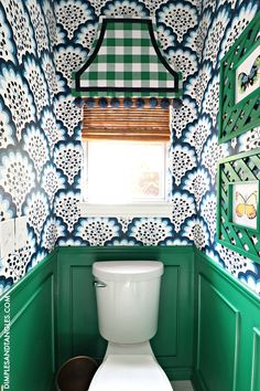 a white toilet sitting next to a window in a green and white bathroom with wallpaper