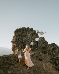 three people climbing up a rocky hill with one woman in a white dress and the other man in a blue shirt