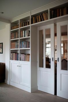 an empty room with white bookcases and doors leading to the living room area