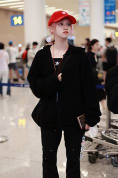 a young woman wearing a red hat and black jacket in an airport terminal with her hand on her hip