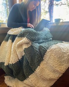 a woman sitting on a window sill with a blanket over her and looking at a laptop