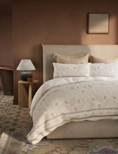 a large bed sitting next to a lamp on top of a wooden table in a bedroom