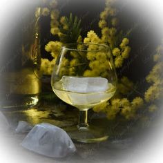 a glass filled with white wine next to yellow flowers