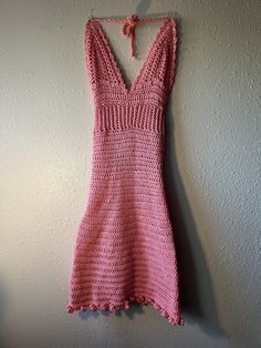 a pink crocheted dress hanging on a wall