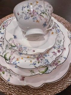 a stack of plates with flowers on them sitting on a wooden table next to a cup and saucer