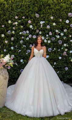 a woman in a white wedding dress standing next to a flowered wall with flowers