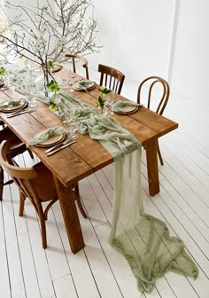 a wooden table topped with lots of plates and chairs next to a vase filled with flowers