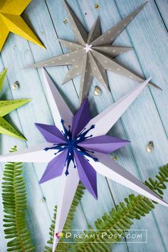 three paper stars sitting next to each other on top of a wooden table with fern leaves