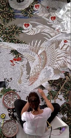 a woman sitting in front of a wall covered in glass mosaics and flowers, with her hands on her head