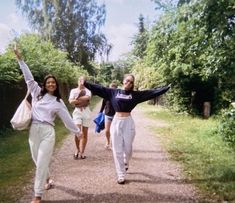 two women walking down a dirt road with their arms in the air and one holding her hands up