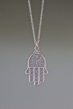 "A beautifully detailed Bali Silver Hamsa filigree charm simply dangles from a delicate silver chain. The chain measures 16\" with an extension to 18\" and is finished with a silver spring ring clasp. Please send a message if a different length chain is desired. The filigree detail in this charm is amazing! Hamsa Hand charm: 16x28mm Total length of pendant: almost 1 1/4\" Silver chain: 1mm All silver is sterling. As the owner, maker, designer, and curator of this shop, I take great pride in prov Silver Necklaces With Intricate Dangle Design, Intricate Dangle Necklace For Gifts, Ornate Dangle Necklace Gift, Delicate Silver Filigree Necklace, Silver Filigree Symbolic Jewelry, Delicate Sterling Silver Filigree Necklaces, Delicate Sterling Silver Filigree Necklace, Nickel-free Ornate Sterling Silver Necklaces, Hamsa Necklace Silver