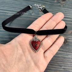 Gothic Black Velvet Choker Necklace with Red & Silver Heart Shaped Pendant Length: 13" + 2" extender  Handmade  Embrace your dark and mystical side with this Gothic Black Velvet Choker Necklace. Handcrafted with intricate details, it features a captivating red and silver heart-shaped pendant adorned with a floral rose motif and the iconic evil eye or third eye symbol. This necklace exudes a whimsical yet edgy vibe, perfect for those who resonate with the goth and wiccan aesthetic. Crafted with care, this unique piece of jewelry makes an enchanting gift for the witchy woman in your life or a bewitching addition to your own collection. Elevate your mystical style with this one-of-a-kind Gothic Black Velvet Choker Necklace. Third Eye Symbol, Wiccan Aesthetic, Mystical Style, Black Velvet Choker Necklace, Velvet Choker Necklaces, Black Velvet Choker, Eye Symbol, Rose Motif, Heart Shaped Pendant