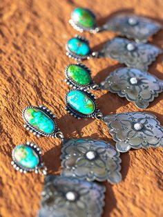 a group of necklaces with turquoise and green stones on them sitting in the sand