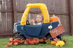 a little boy sitting in a toy truck with fall decorations on the grass and pumpkins