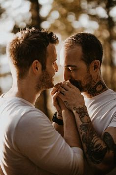 two men standing next to each other with tattoos on their arms and chest, looking at each other