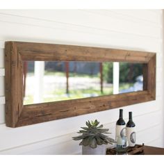 a wooden mirror hanging on the side of a wall next to a bottle of wine