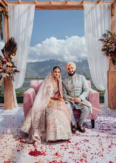 a bride and groom sitting on a pink couch in front of an arch with flowers