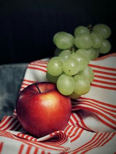 an apple and grapes sit on a striped cloth