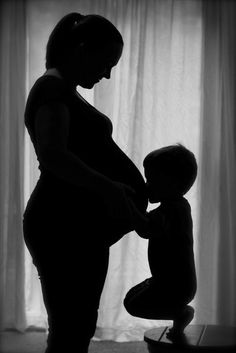 the silhouette of a pregnant woman holding her child's hand while standing in front of a window