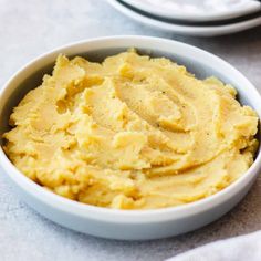 a white bowl filled with mashed potatoes on top of a table next to another plate