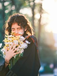 a woman holding flowers in her hands and looking at the camera with sunlight shining on her face