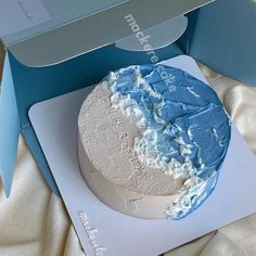 a blue and white cake in a box on a bed with the lid open to show it's frosting