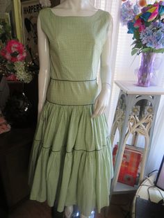 "1950s' cute light olive green/white checkered sleeveless dress, but no label name or size tag.  Dress fabric is cotton, has a left side metal zipper closure, boat neckline, huge 2-level gathered skirt with dark olive green string trim around skirt and waist area.  Would look great with a big puffy petticoat slip underneath the skirt part to make the skirt blossom out.  Dress is in very good condition.  SHOULDERS=15\"   ARMHOLES=16\"   BUST=36 1/2\"  WAIST=28\"  Below WAIST area=34\"  SKIRT BOTT Retro Sleeveless Plaid Dress For Spring, Spring Retro Sleeveless Plaid Dress, Vintage Sleeveless Spring Plaid Dress, Vintage Sleeveless Plaid Dress, Vintage Sleeveless Plaid Summer Dress, Vintage Sleeveless Plaid Cotton Dress, Retro Gingham Plaid Cotton Dress, Vintage Cotton Gingham Plaid Dress, Vintage Gingham Plaid Cotton Dress