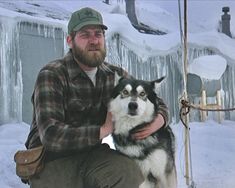 a man is sitting with his dog in the snow